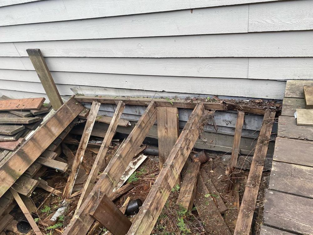 Before: deck surface boards removed exposing rotted, collapsed joists and a water-damaged ledger against the house